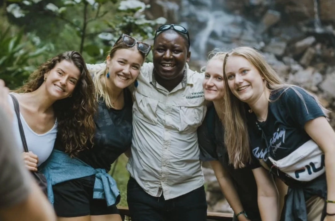 A guide and four visitors smiling together near a waterfall